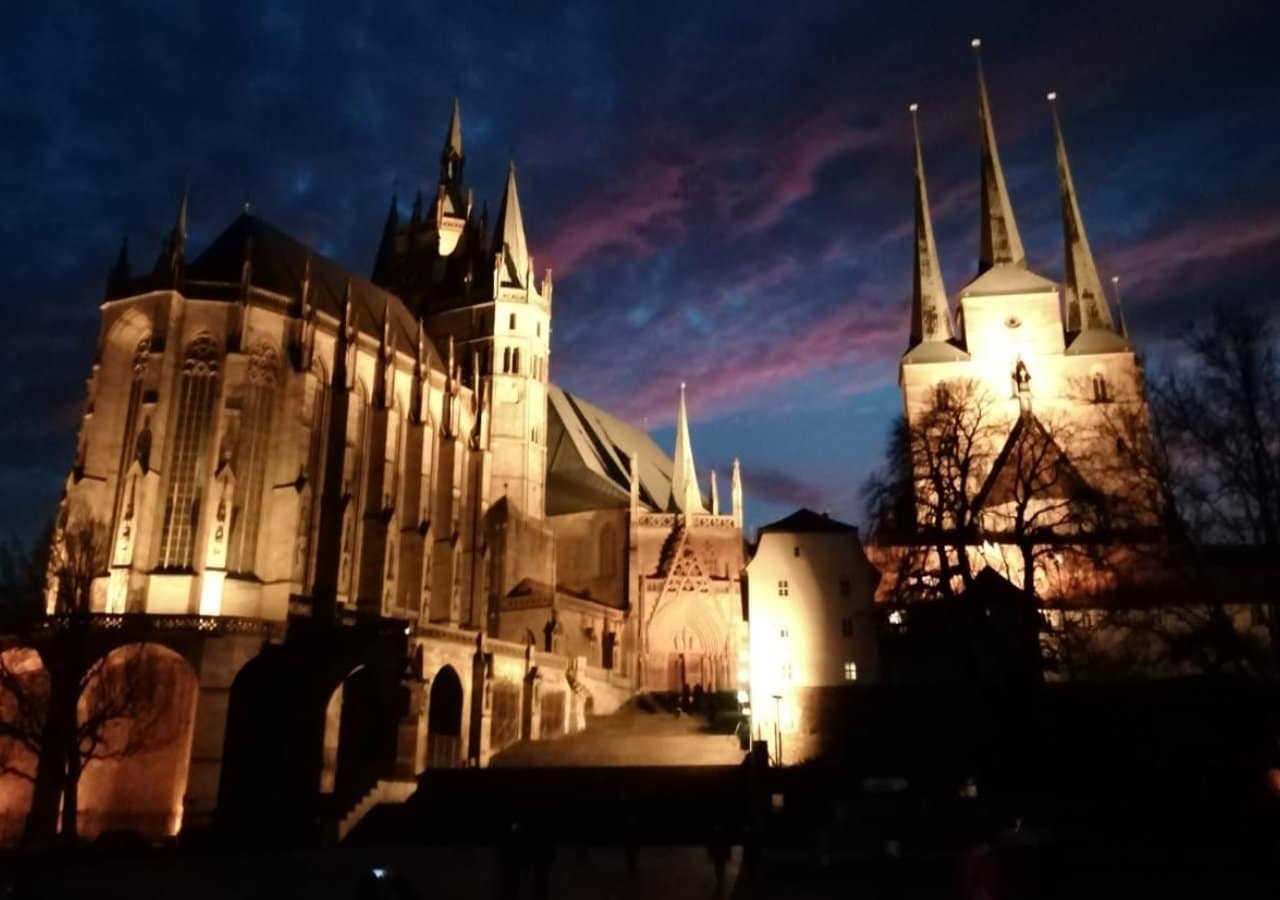 Das Bild zeigt das Augustinerkloster in Erfurt bei Nacht. Der Himmel ist dunkelblau und an der Außenfassade des Klosters leuchten helle Lichter auf.